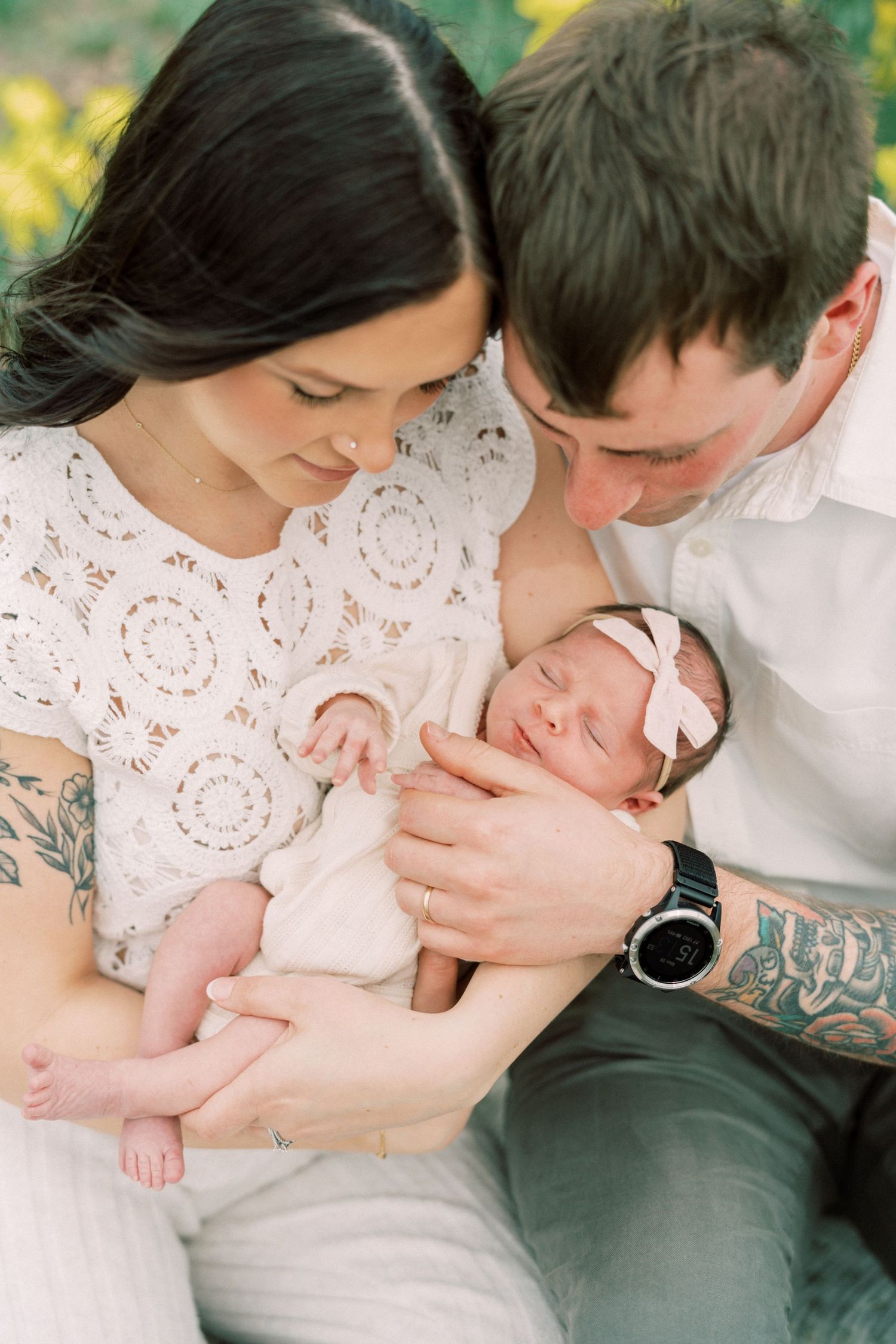 A couple holds and gazes lovingly at their newborn baby wearing a white bow headband.
