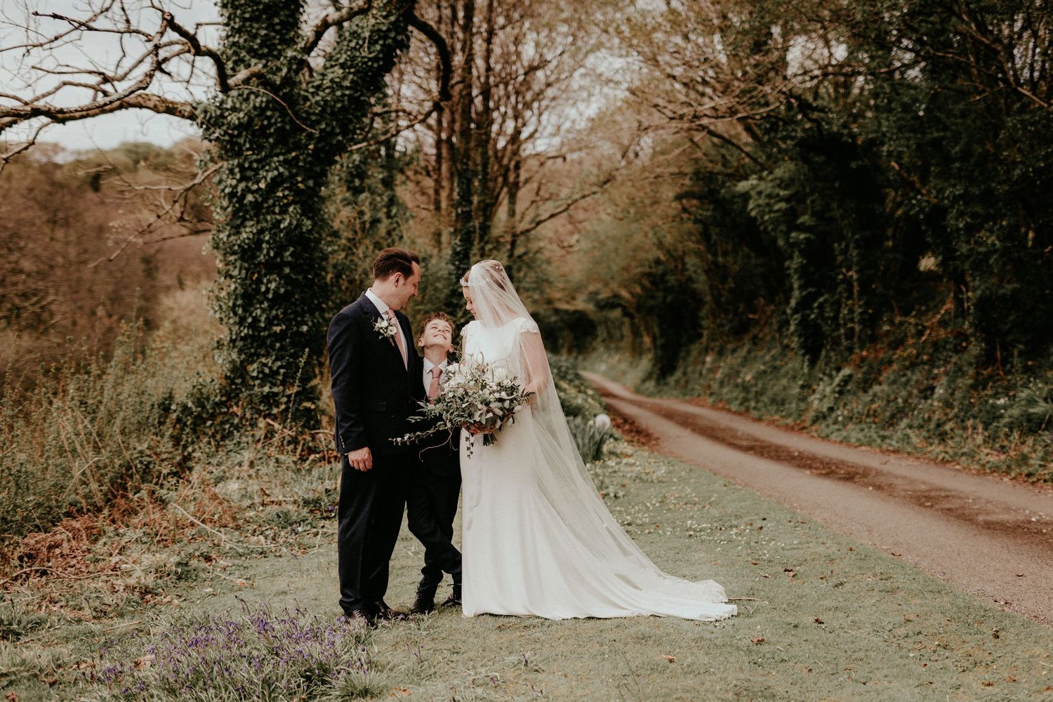 A couple in wedding attire share a kiss under blooming cherry blossoms in an outdoor garden setting.