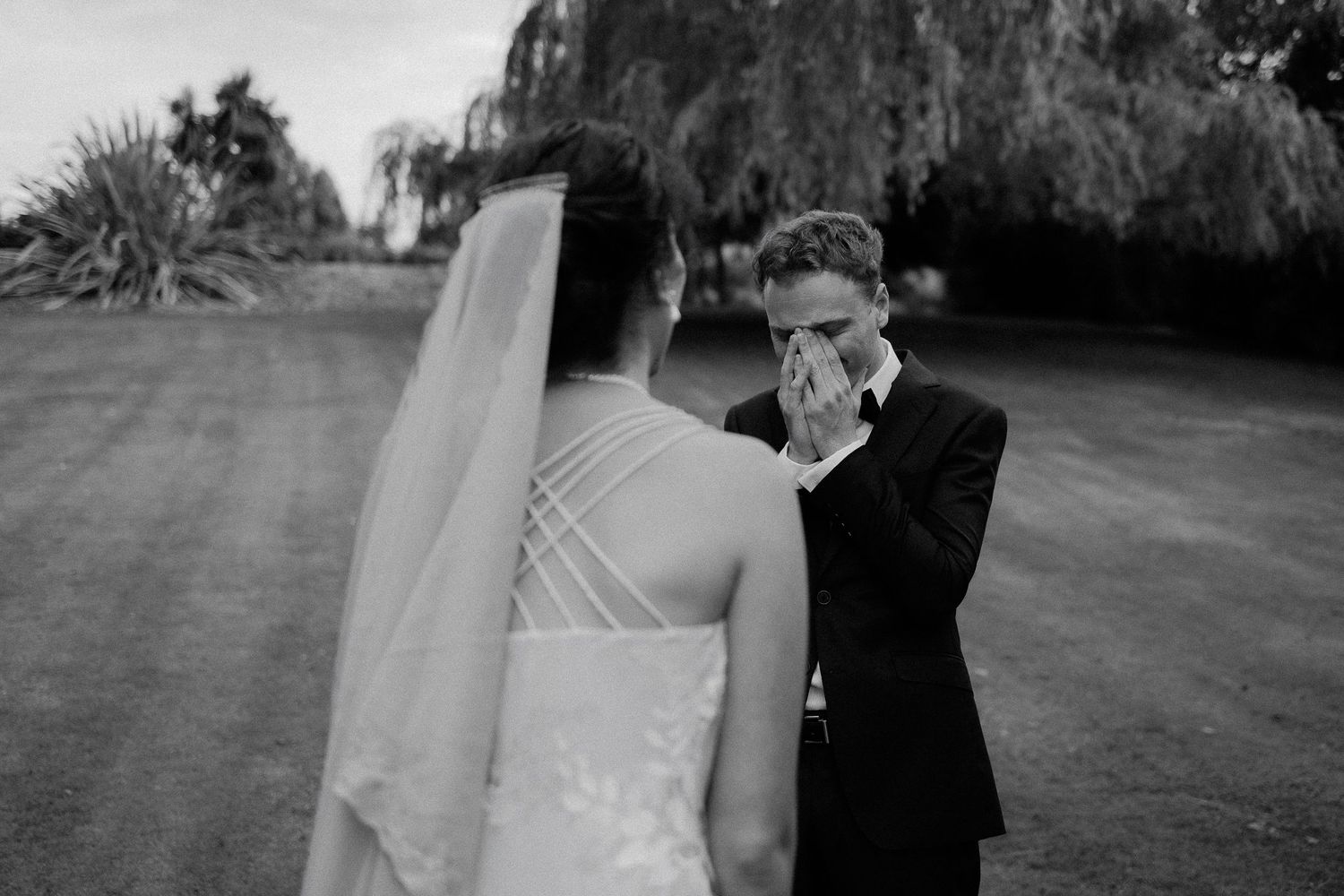 A tender black and white wedding photo moment between a bride in a white gown and another person outdoors.