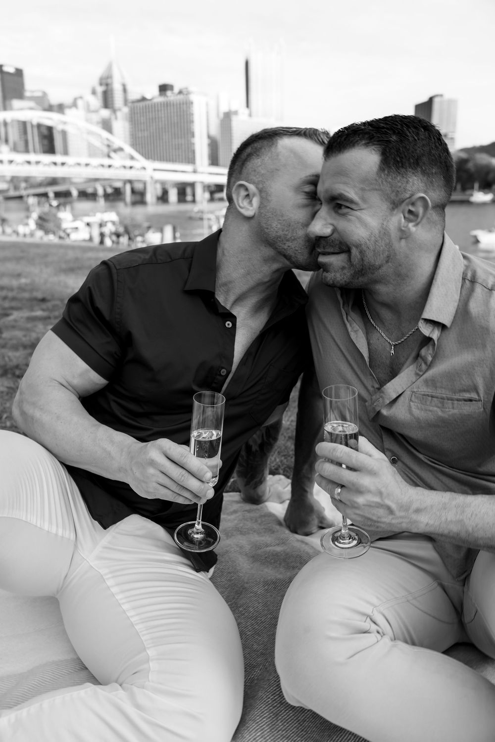 A romantic couple sharing champagne and an intimate moment by the Pittsburgh skyline.
