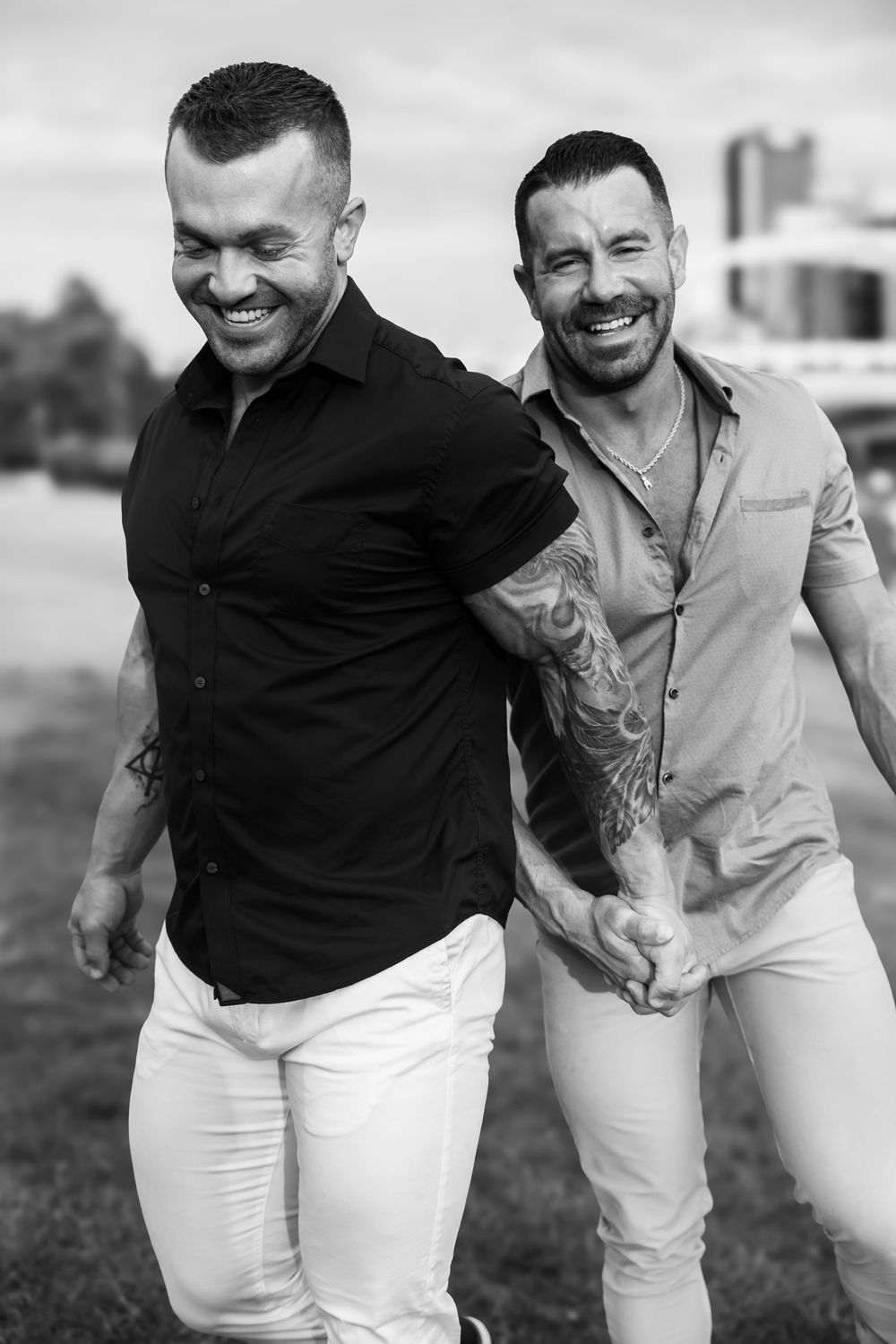 Candid black and white photo shows two men in casual attire laughing and walking together outdoors.