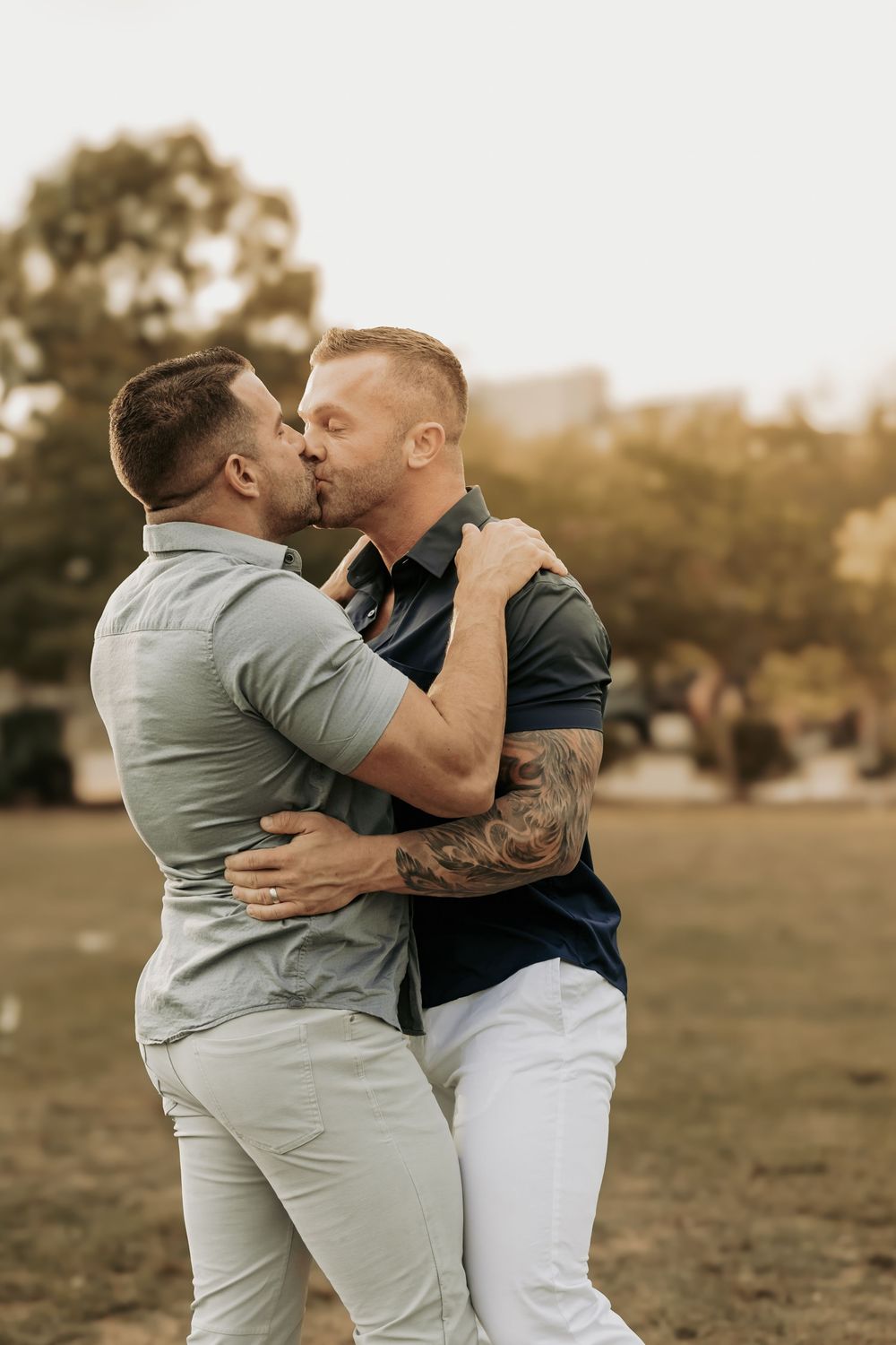 Two people sharing a romantic kiss in a park during sunset as they embrace each other affectionately.