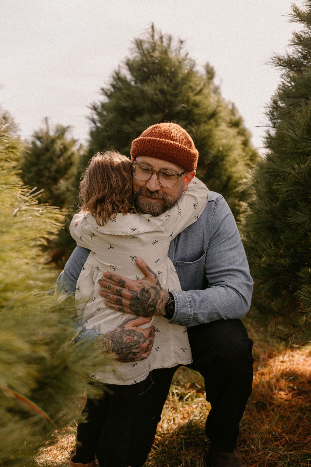 Outdoor tender moment at a Christmas tree farm with evergreen trees in background.