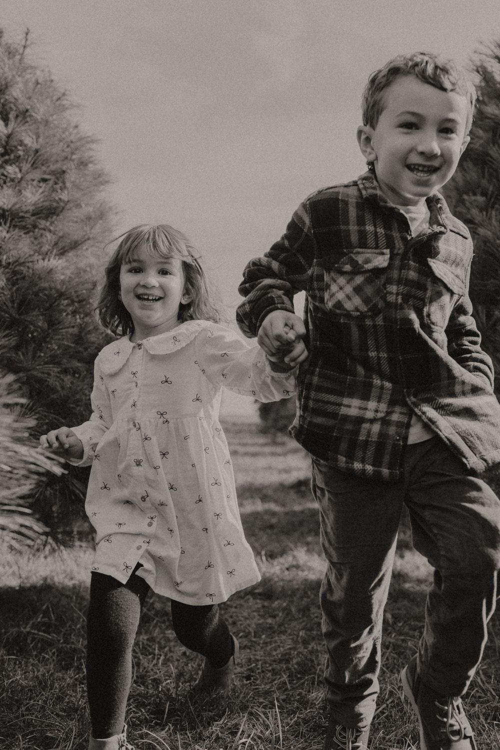 Two children running and laughing together outdoors in black and white.
