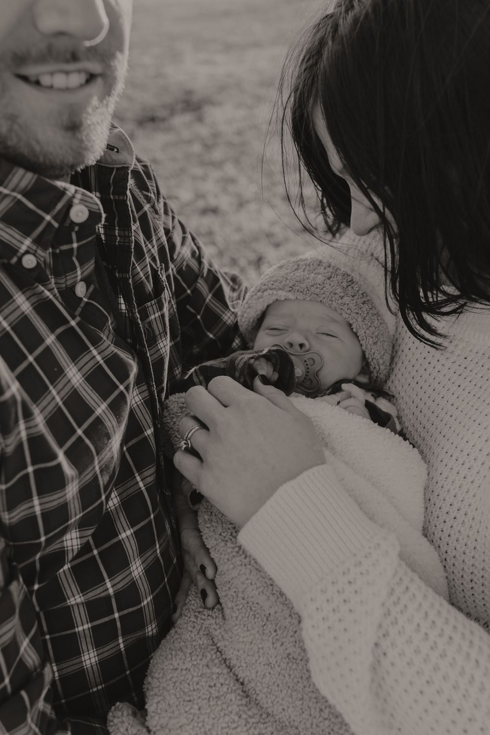 Black and white photo of a newborn baby being cradled in a cozy blanket outdoors.