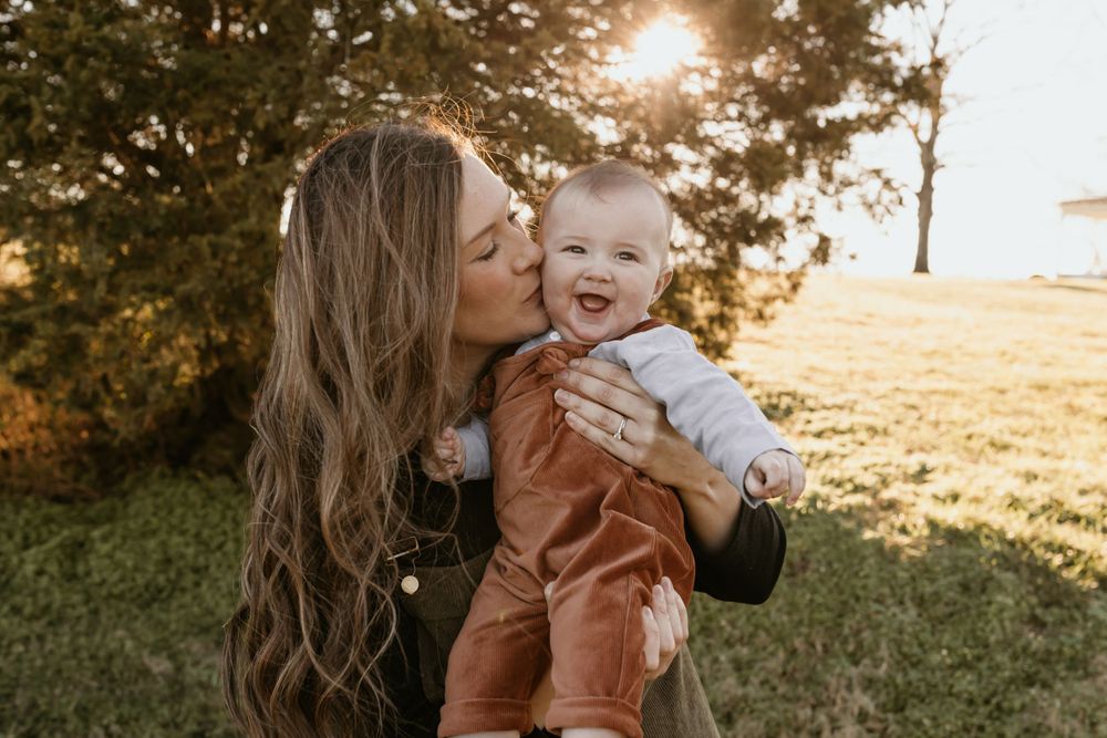 A tender outdoor family moment captured during golden hour in a sunlit field.