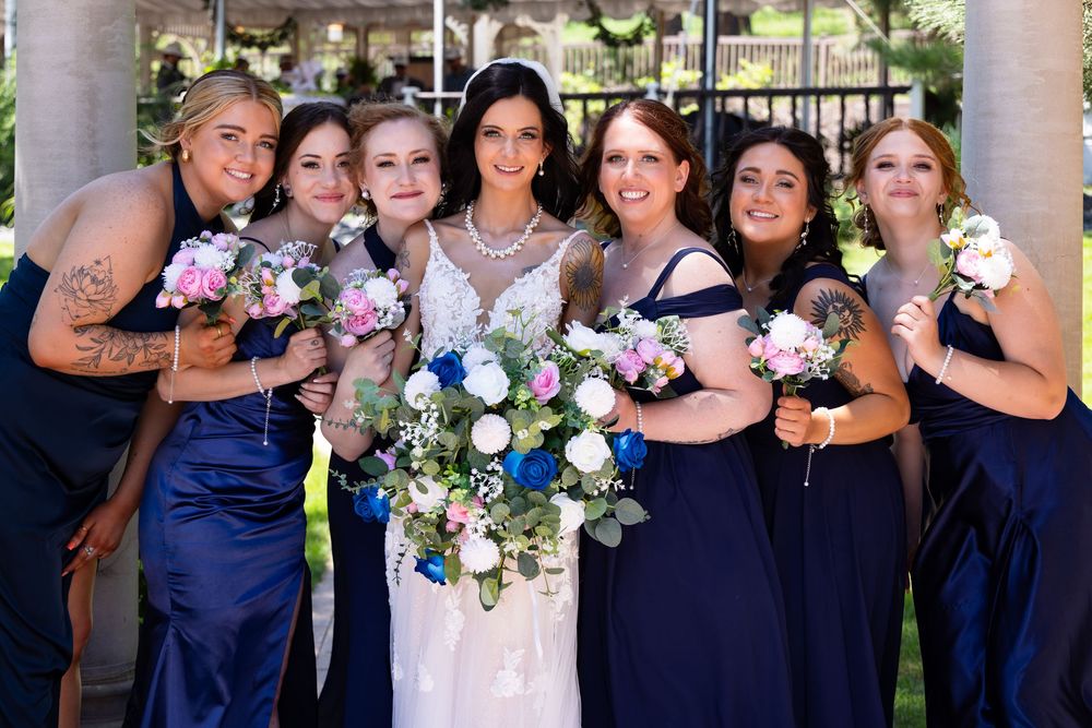 Bridesmaids in matching navy blue dresses pose in a garden setting.