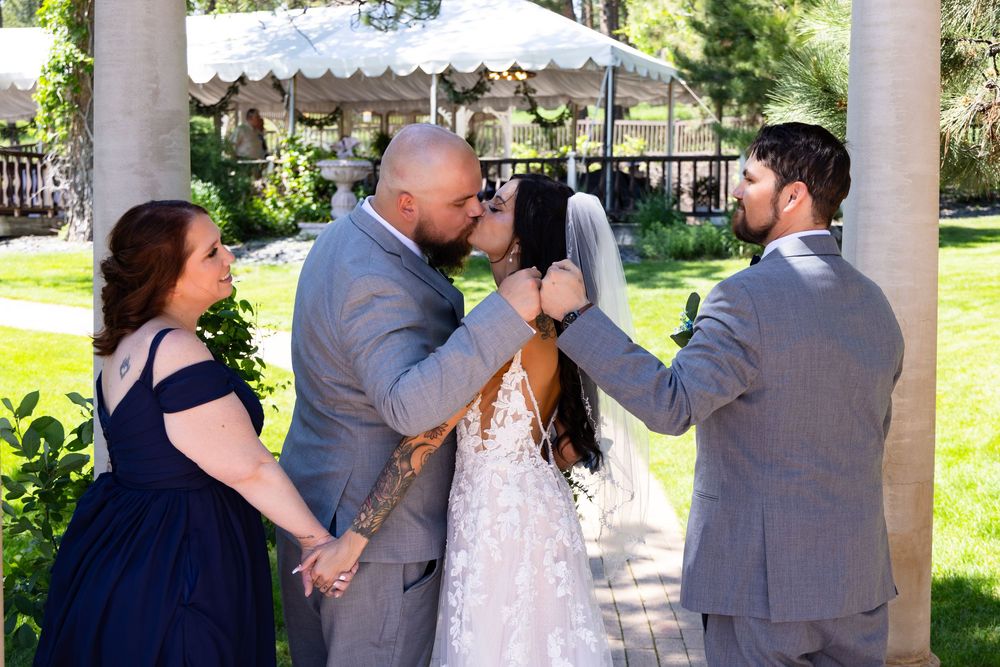 Wedding party walking and talking together under a white covered outdoor pavilion on a sunny summer day.
