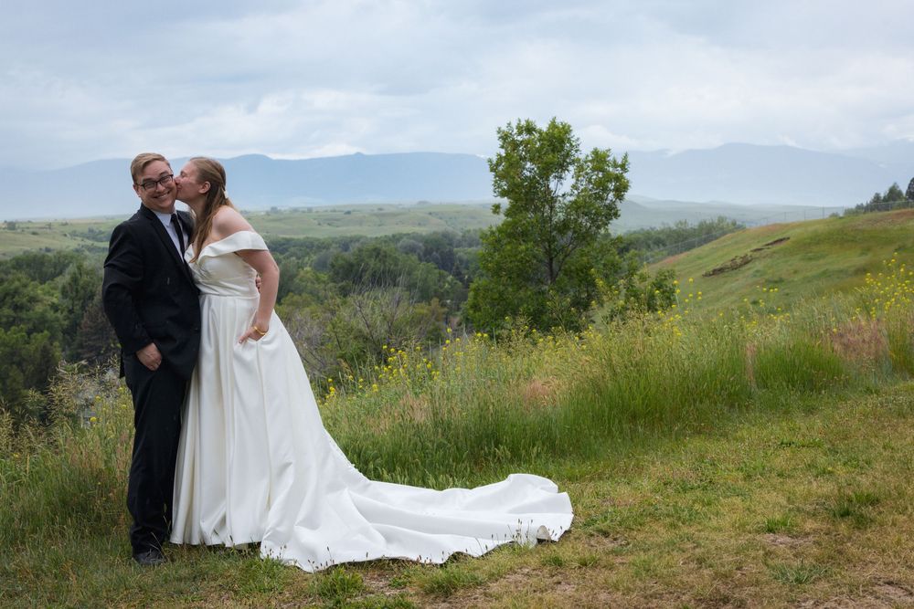 A couple shares an intimate moment on a hilltop meadow with rolling mountains in the background.