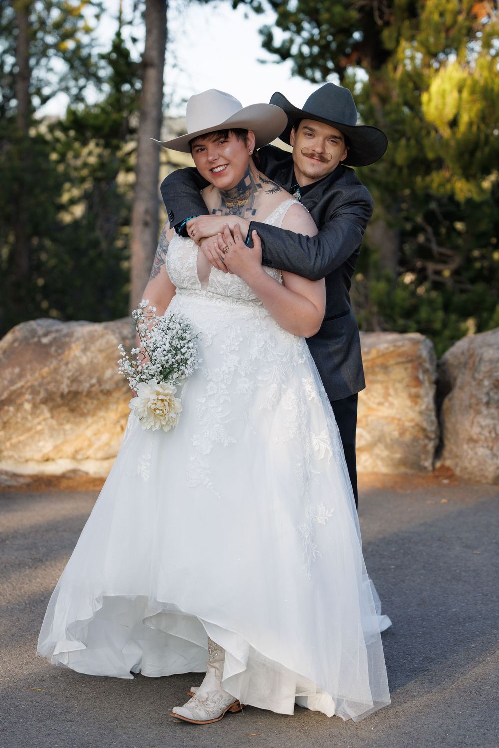 A joyful couple in matching cowboy hats and western attire pose together on their wedding day.