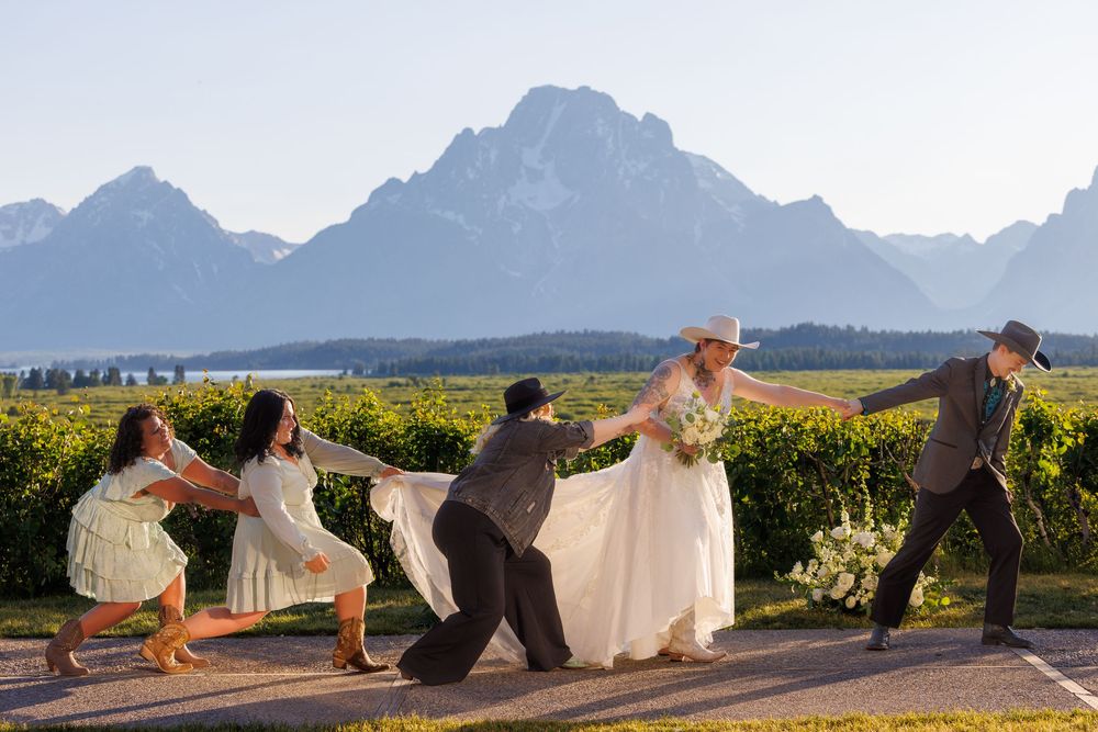Wedding party posing playfully in a line against a backdrop of Grand Teton mountains and wildflower fields.
