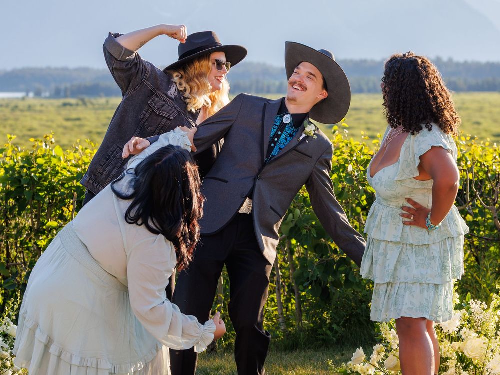Wedding party in cowboy hats and formal wear strike playful poses in a sunny flower field.