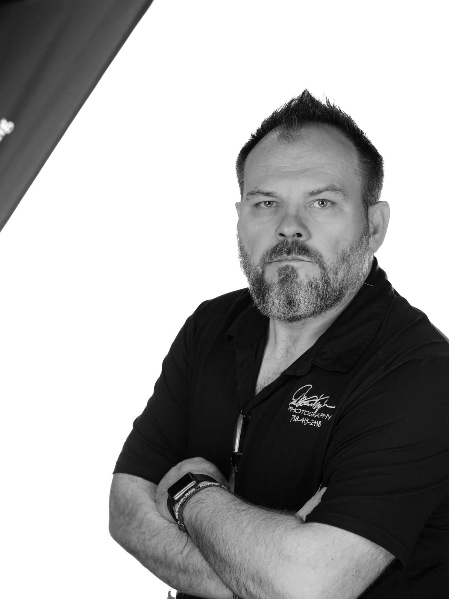 Professional black and white portrait of someone in a black polo shirt with crossed arms and a beard looking to the side.