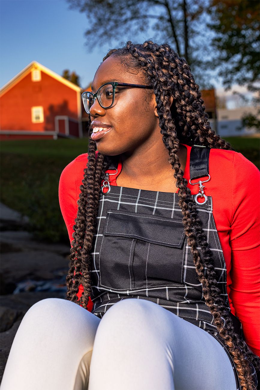 A joyful smile captured in front of a red barn while wearing black overalls and a red top.