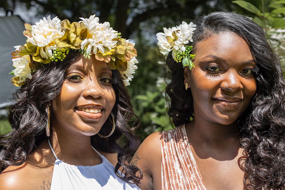 Two people wearing floral crowns and summer dresses at an outdoor celebration.