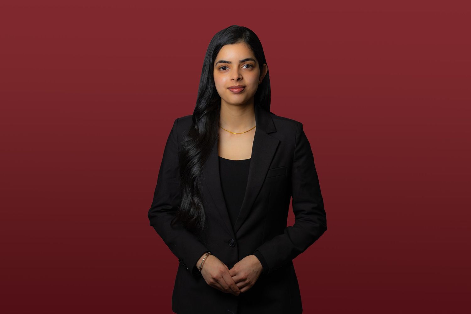 Professional portrait of a person in a black blazer and top standing against a deep red background.