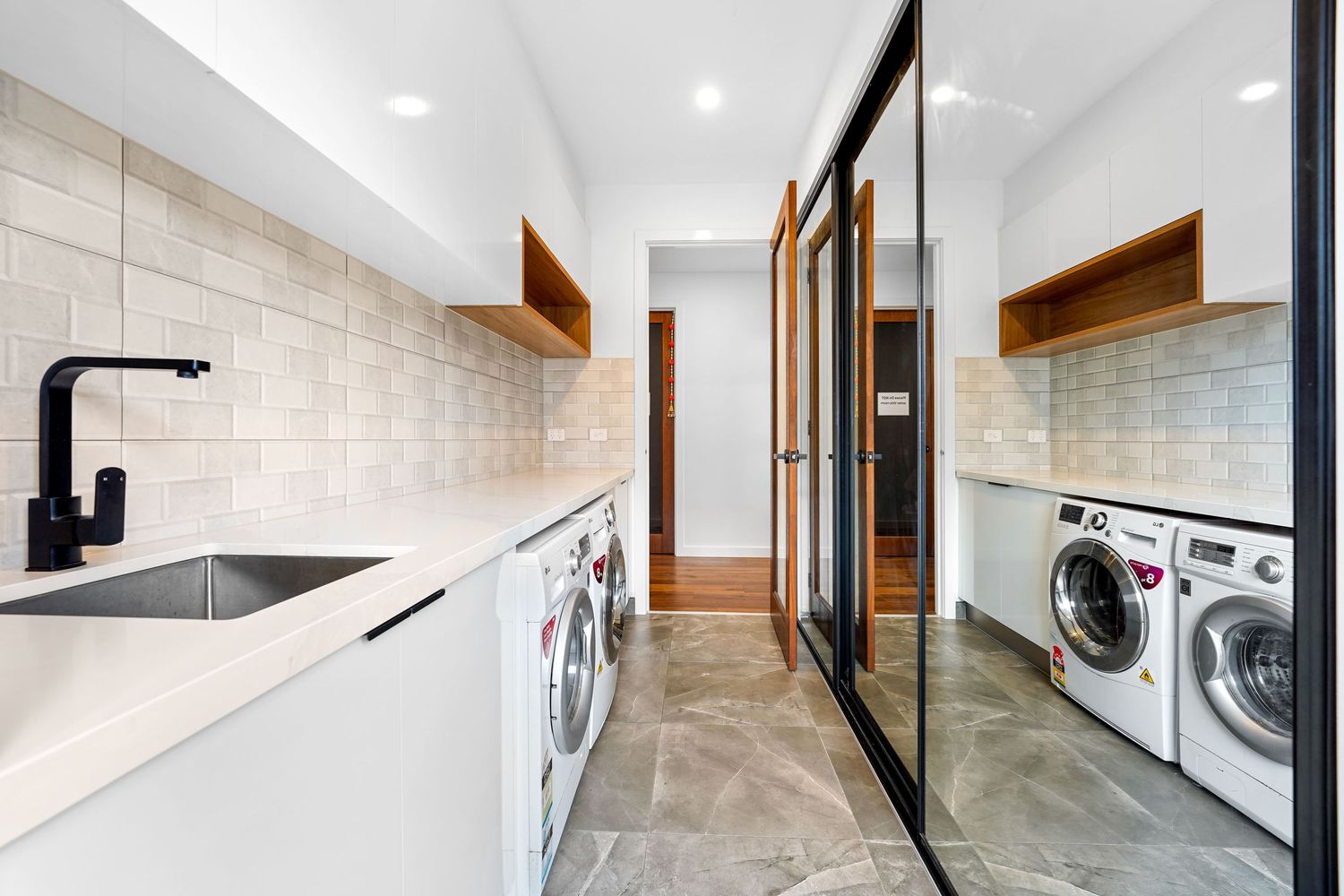 Modern laundry room with white appliances, mirrored closet doors, and white quartz countertops with black fixtures.