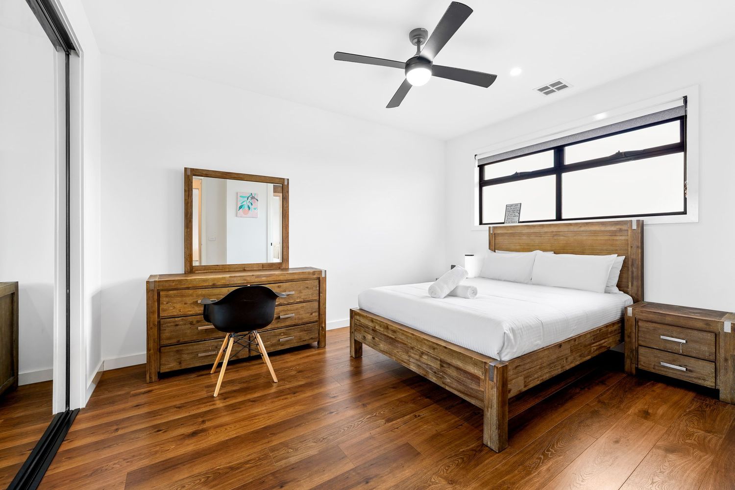 Modern minimalist bedroom with hardwood floors, rustic wooden bed frame, matching dresser, and black accent chair.
