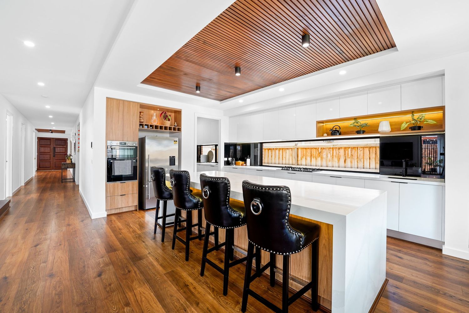 Modern kitchen interior with white countertops, wood flooring, and sleek black bar stools along marble waterfall island.