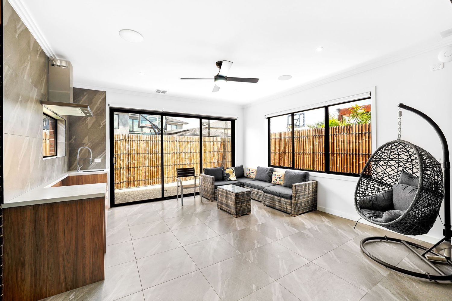 Modern living room with gray sectional sofa, hanging egg chair, and bamboo privacy screens leading to outdoor space.