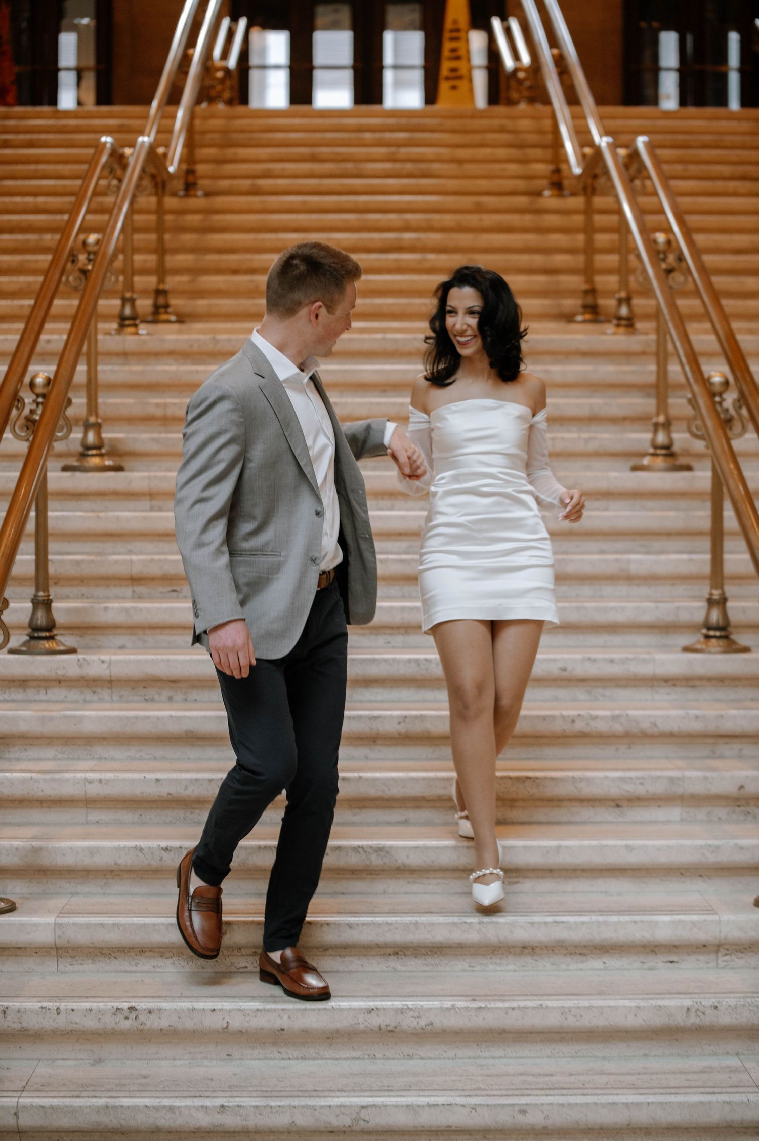 A couple in wedding attire pose playfully on marble stairs in a series of candid moments during their photo session.