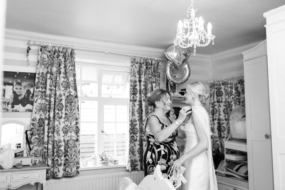 Black and white photograph of a person looking down at a dog in a home interior with floral curtains and a chandelier.