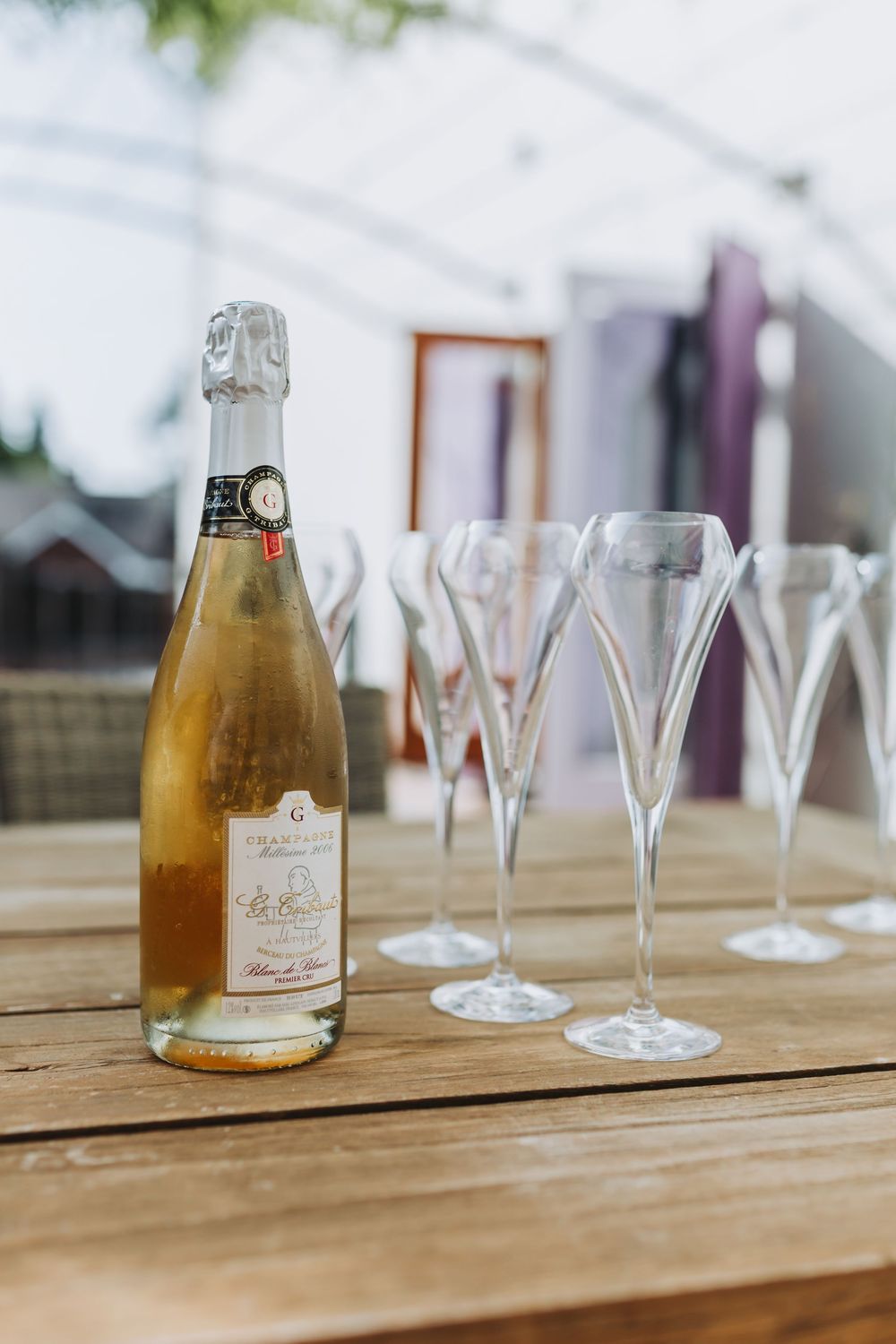 A bottle of champagne sits beside empty flute glasses on a wooden table in an elegant setting.