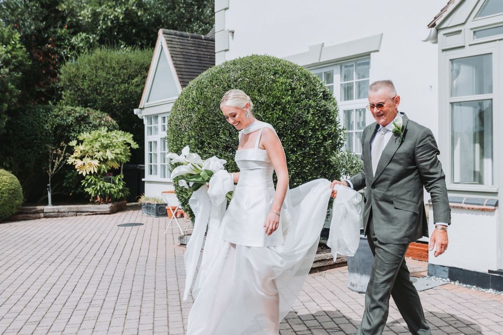 Elegant outdoor wedding scene with bride in white gown and groom in charcoal suit walking together on wooden deck.
