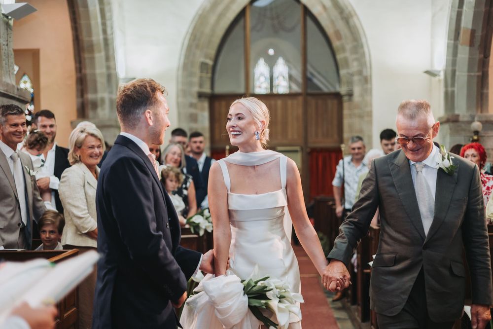 A newly married couple exits a church while guests gather on both sides to celebrate their wedding ceremony.