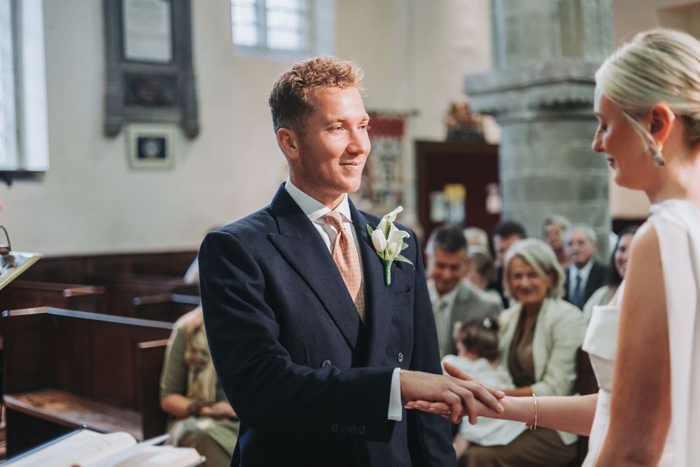 A couple exchanges wedding rings during their ceremony in a traditional church setting with guests watching in the background.
