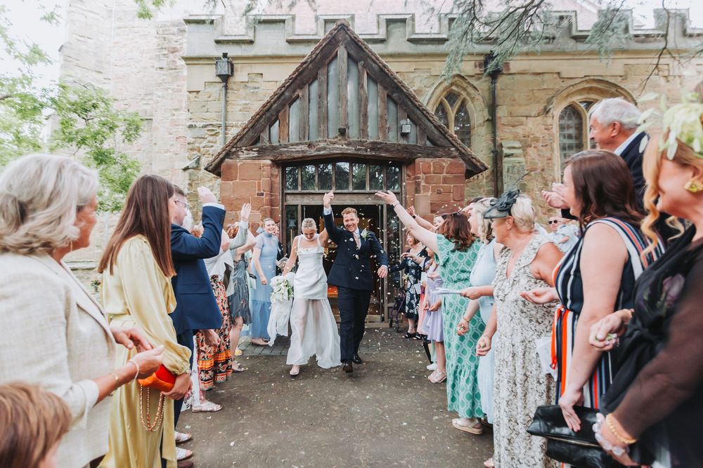 Wedding guests dancing and celebrating at an outdoor reception with string lights hanging above.