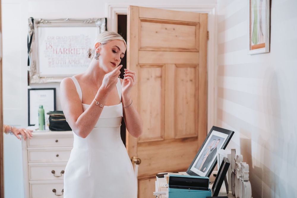 Woman in white wedding dress applies makeup in a mirror while getting ready for her special day.