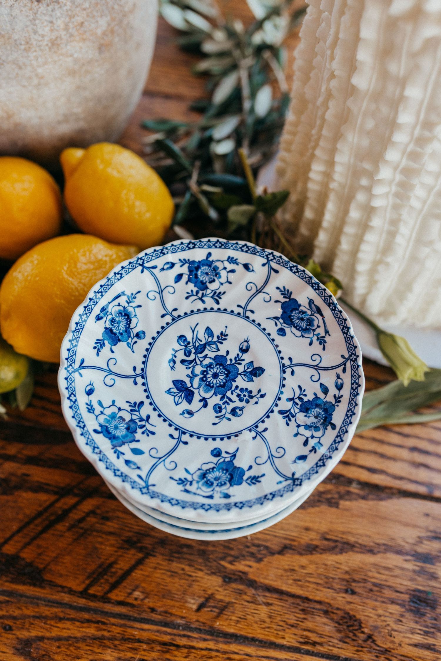 Blue and white floral china plate displayed on wooden table with fresh lemons and greenery in background.