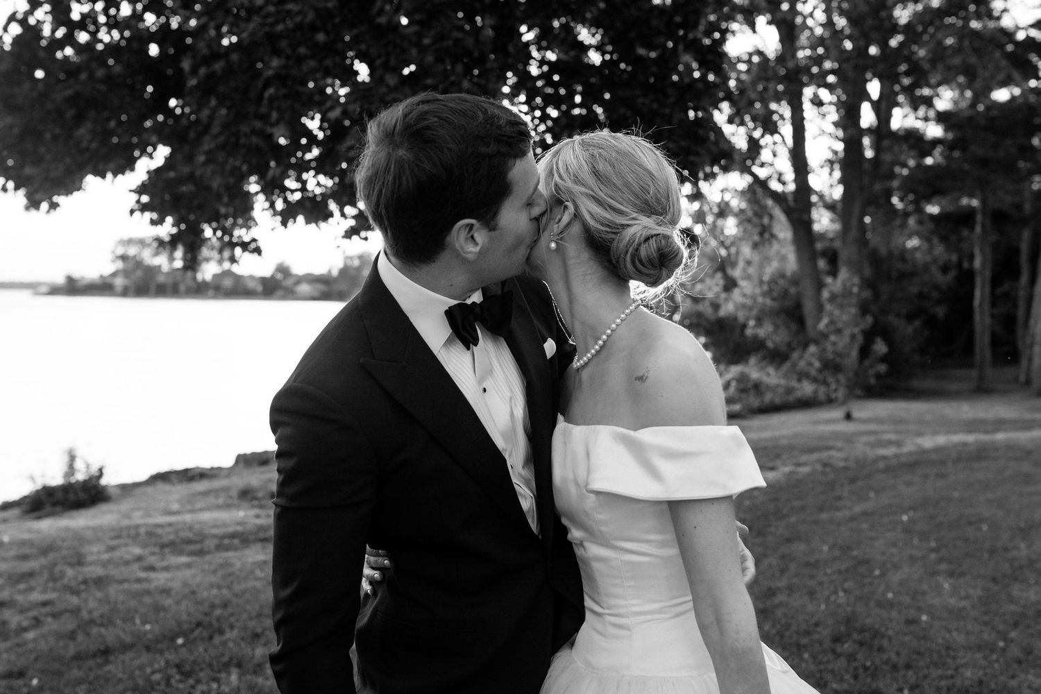 A black and white romantic wedding portrait of newlyweds in an outdoor lakeside setting.