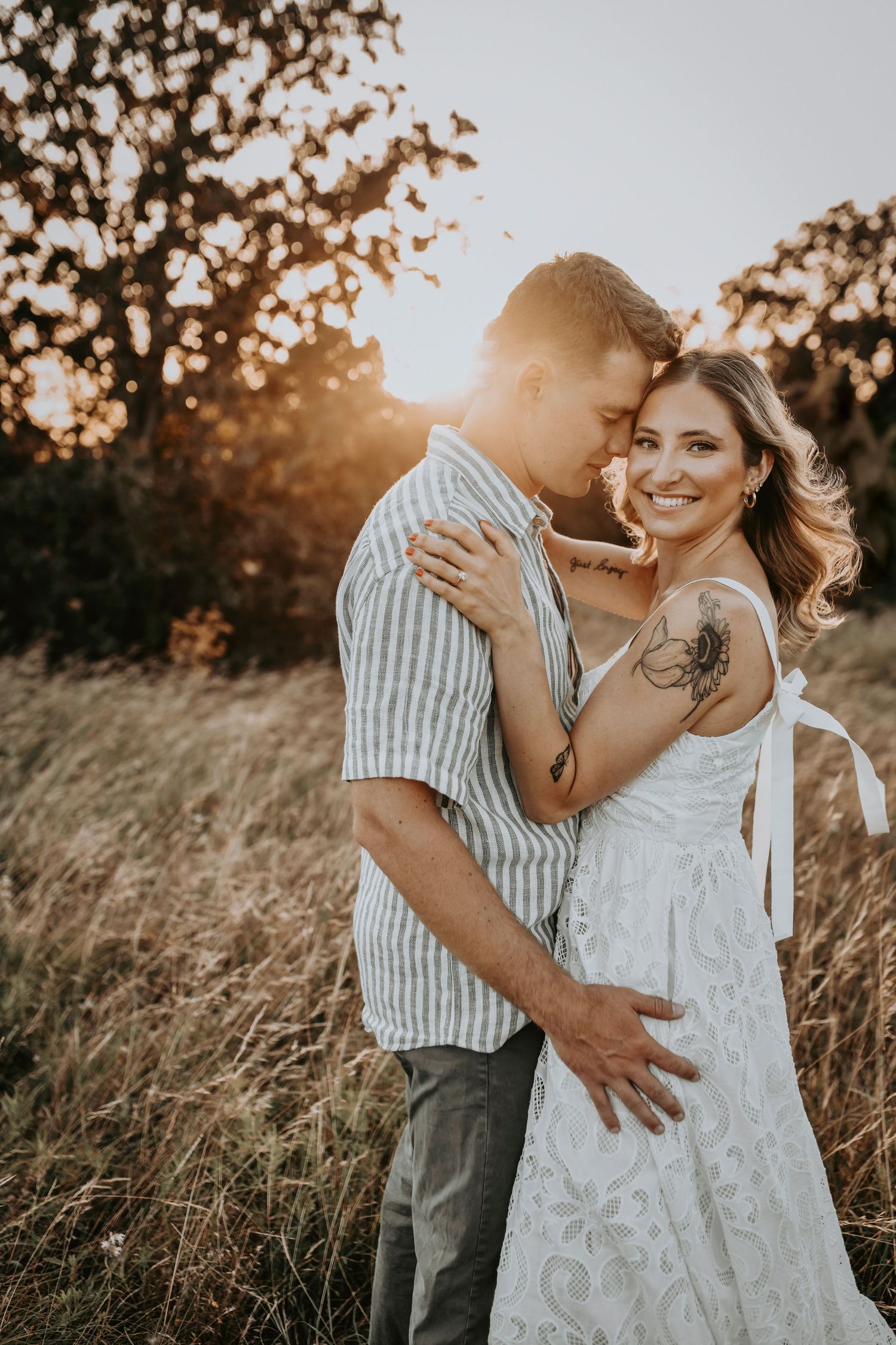 Sunset light beaming behind a couple sharing a forehead kiss in golden grass