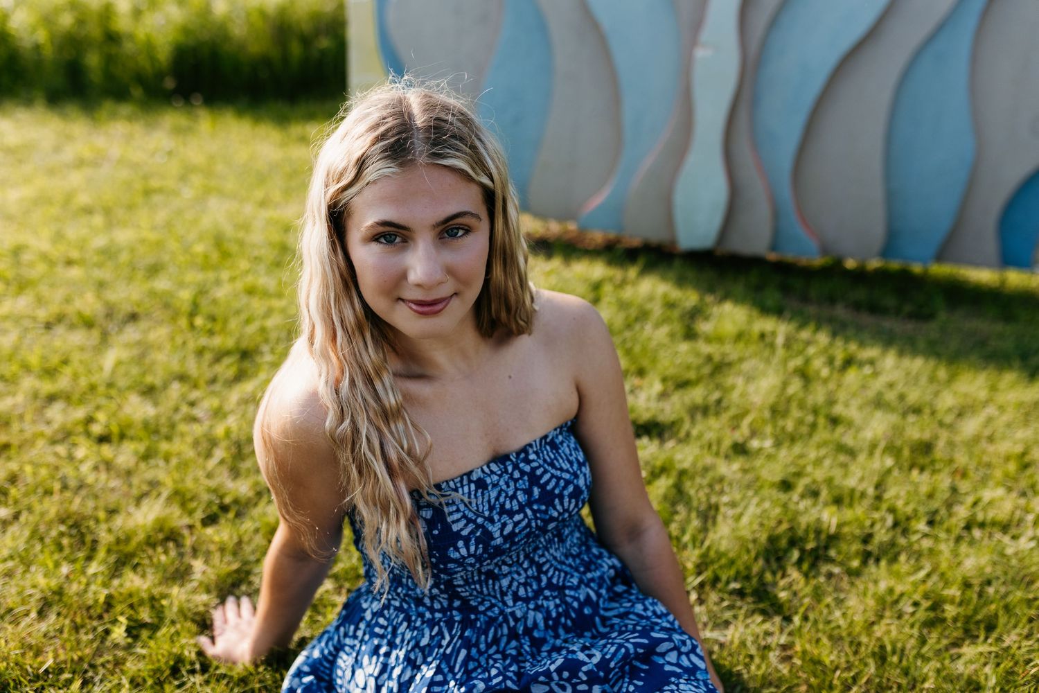 A person in a blue polka dot dress sits in a sunny garden with green grass in the background.