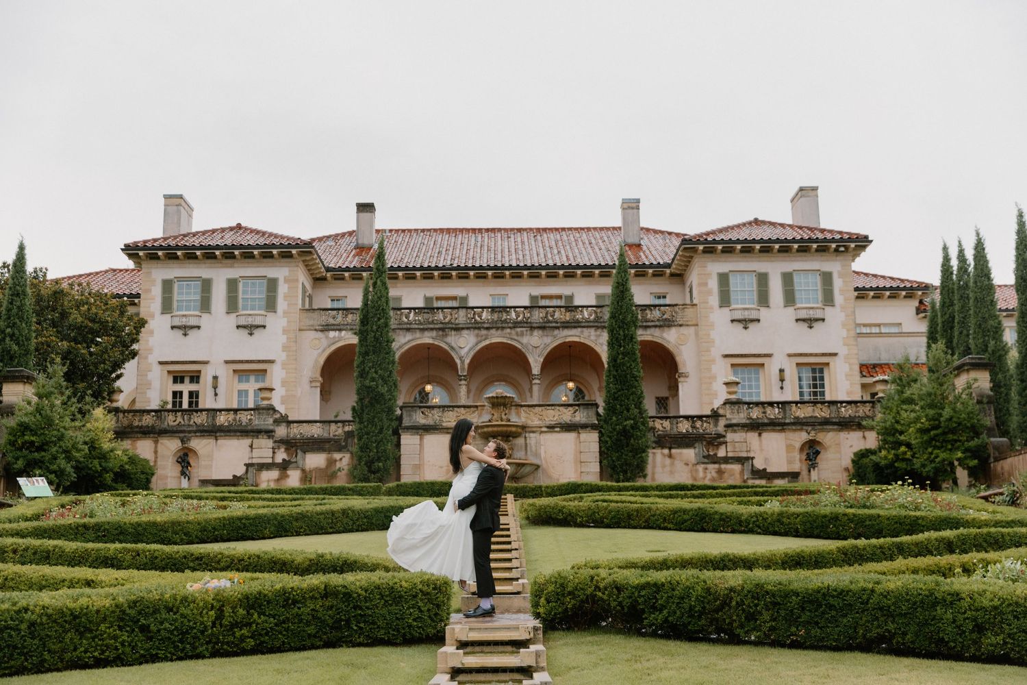Panoramic view of a historic Mediterranean villa with manicured gardens and cypress trees on a sunny day.