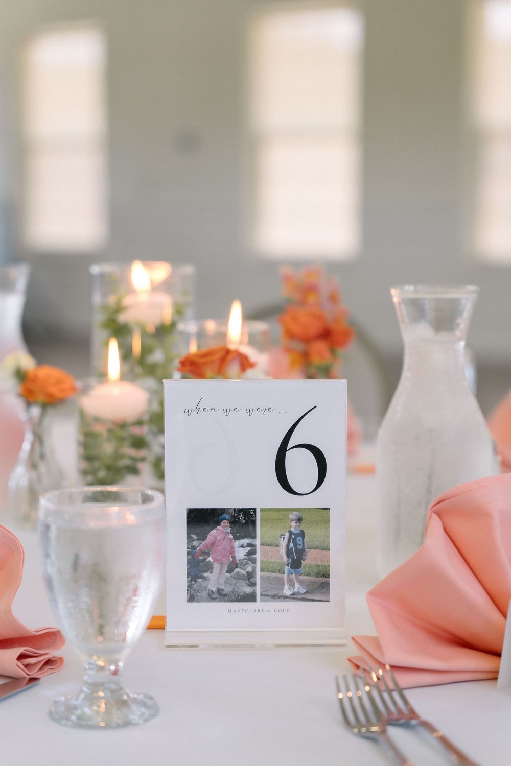 Elegant table setting with orange roses, peach napkins, white candles and photo table numbers at a wedding reception.