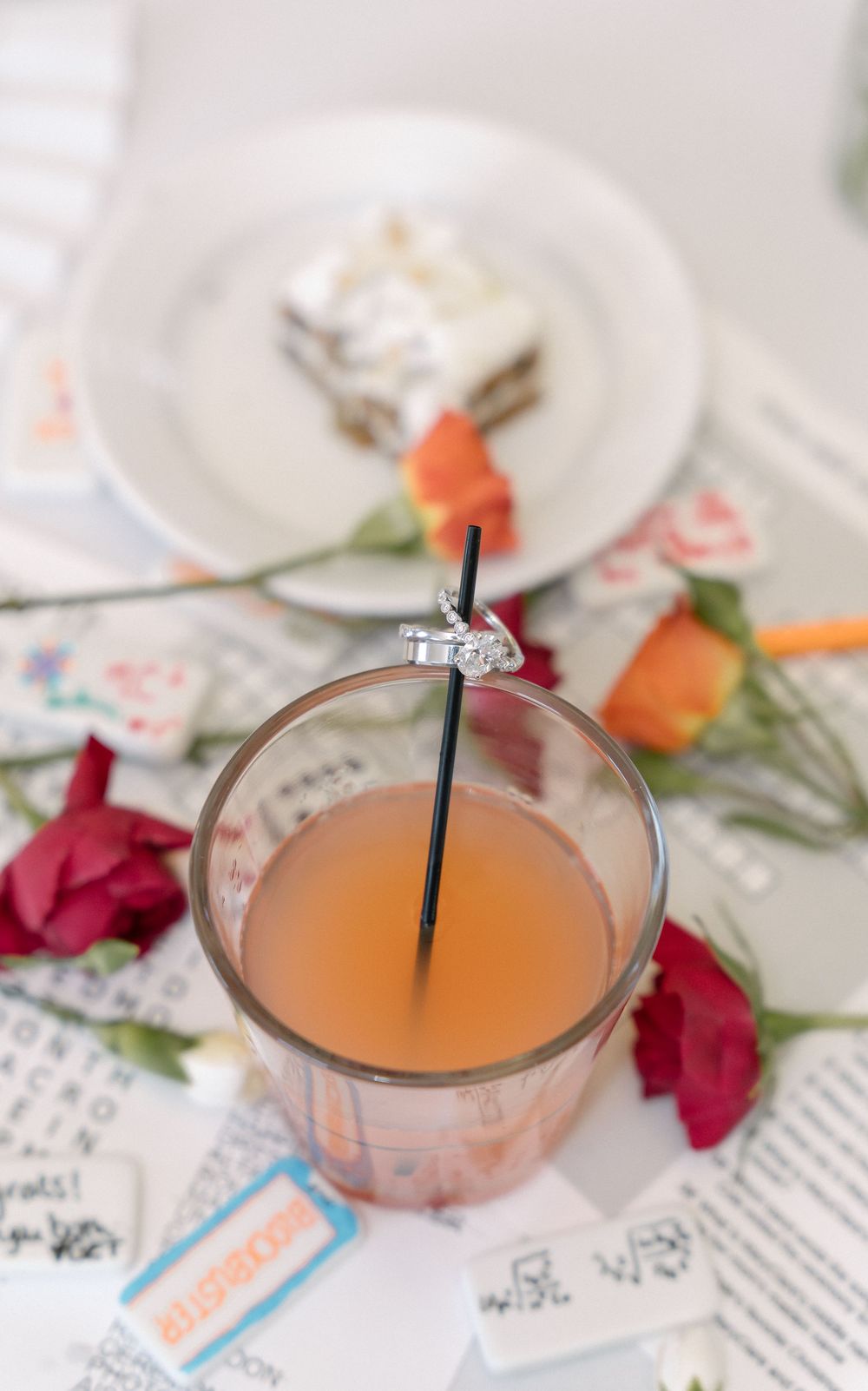 A pink cocktail garnished with red roses sits on table with scattered notes and cards.