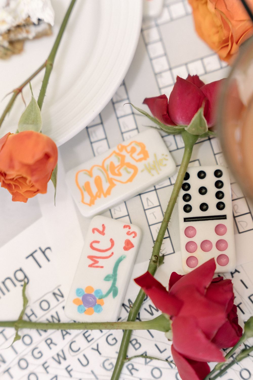Domino pieces and handwritten cards decorated with roses in orange and deep red colors.
