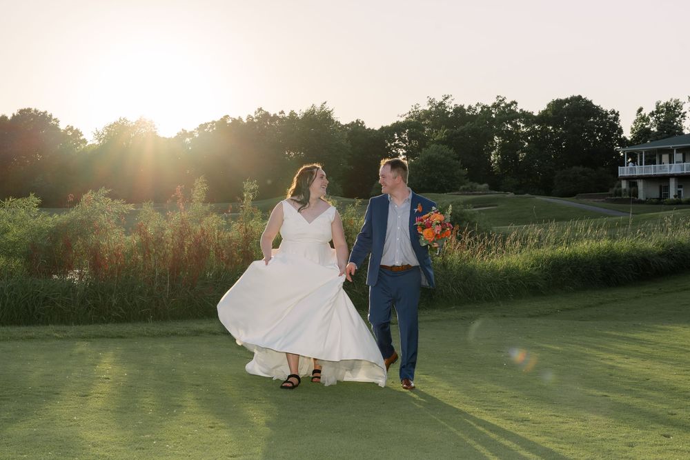 A couple walks together on a grassy lawn during golden hour sunset with lens flare in the background.