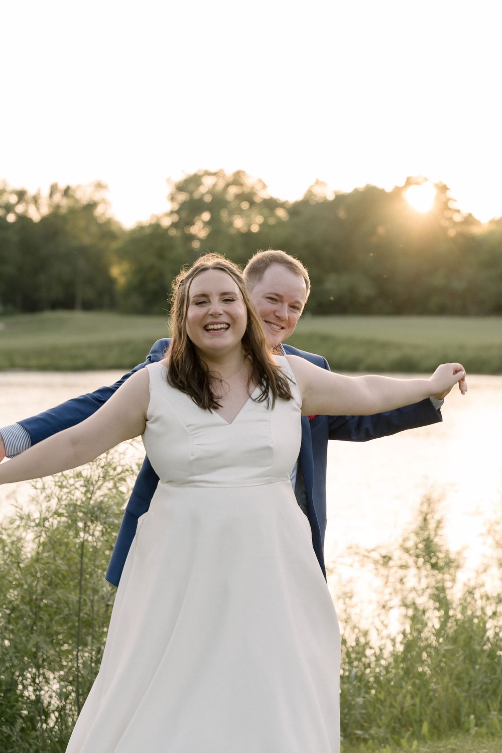 Joyful candid moment of newlyweds posing with arms outstretched against a sunset backdrop.
