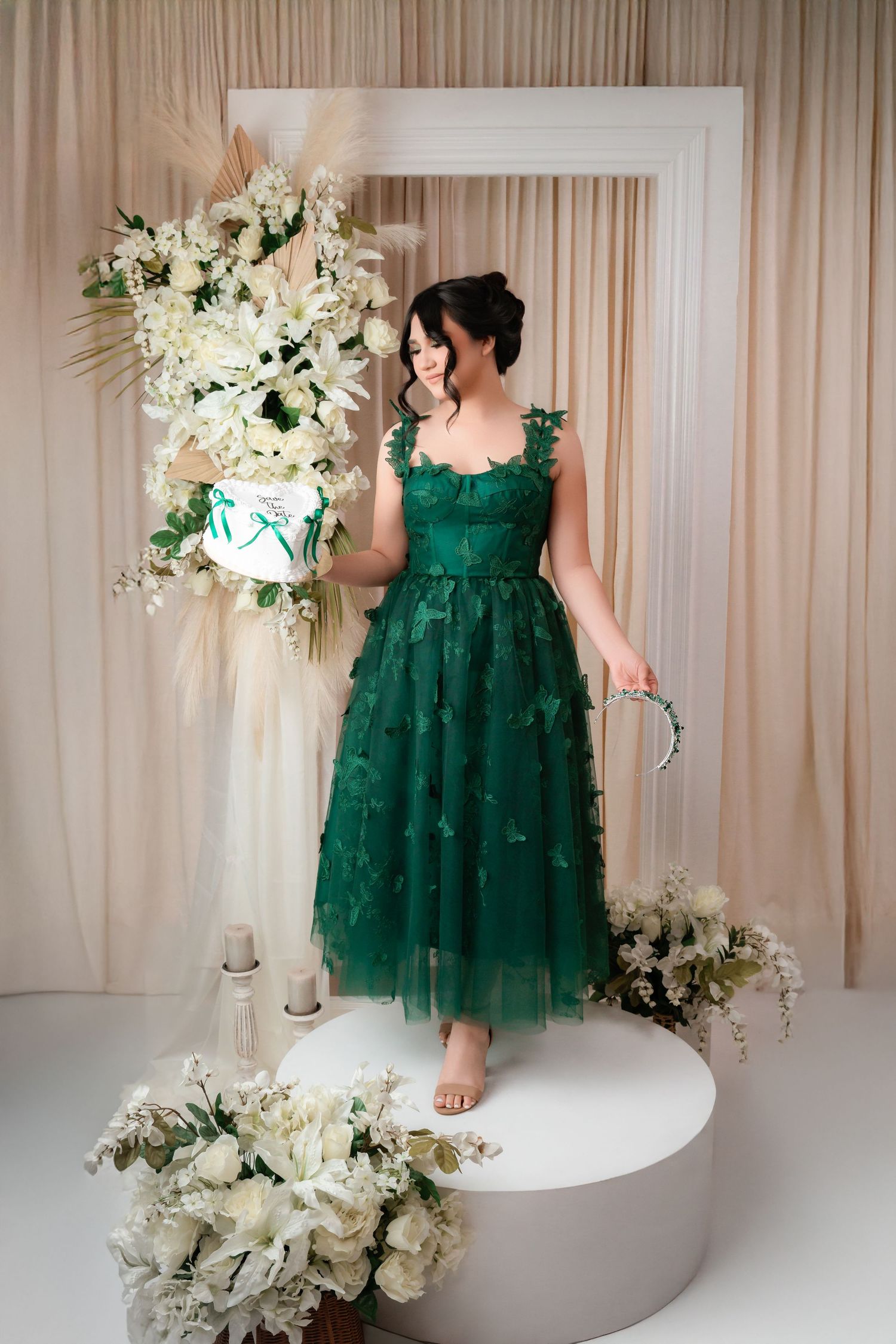 Elegant emerald green tulle dress with floral appliques stands out against a white backdrop with luxurious floral arrangements.