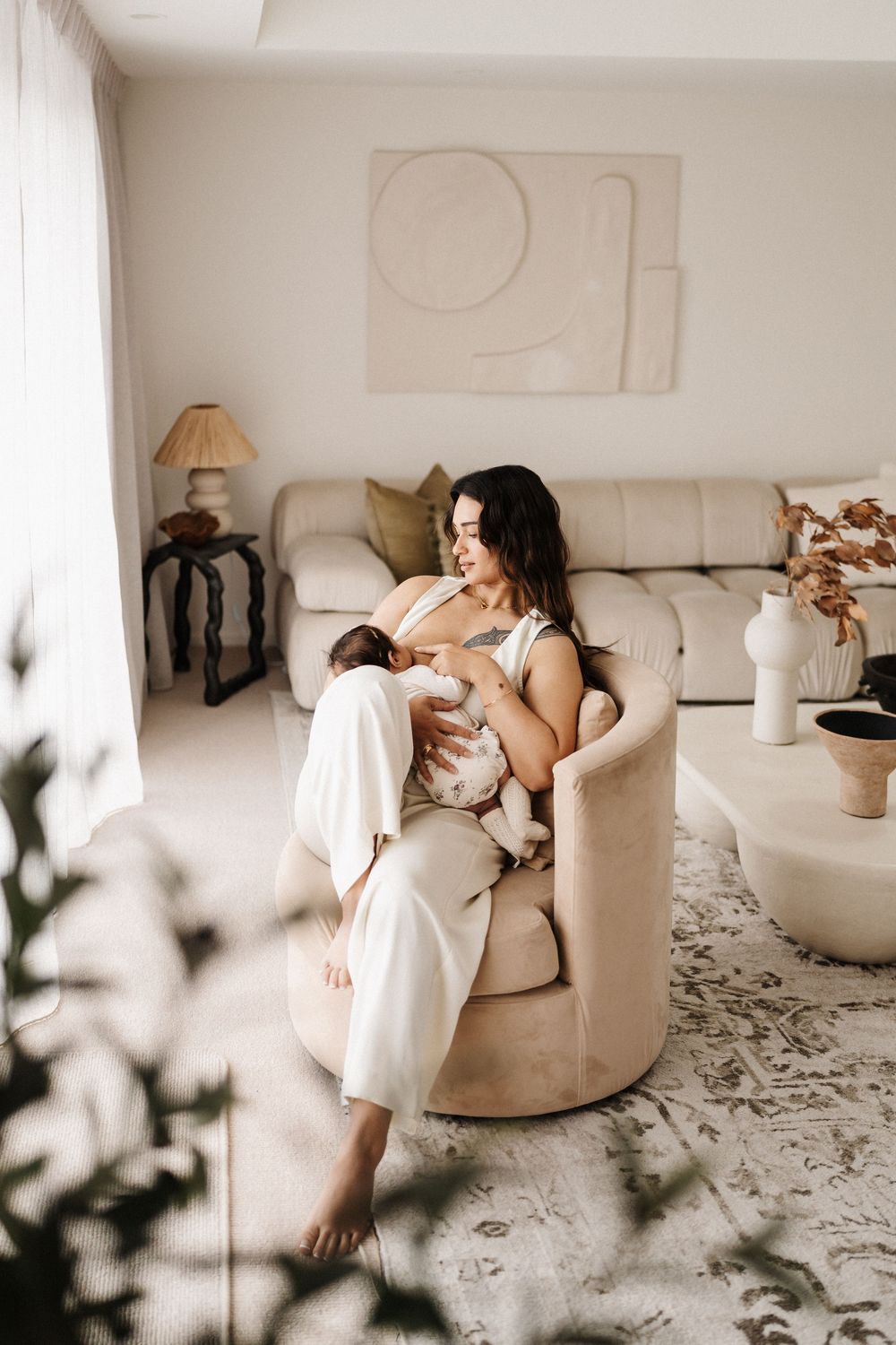 Person lounging in beige armchair with baby in minimalist living room setting.