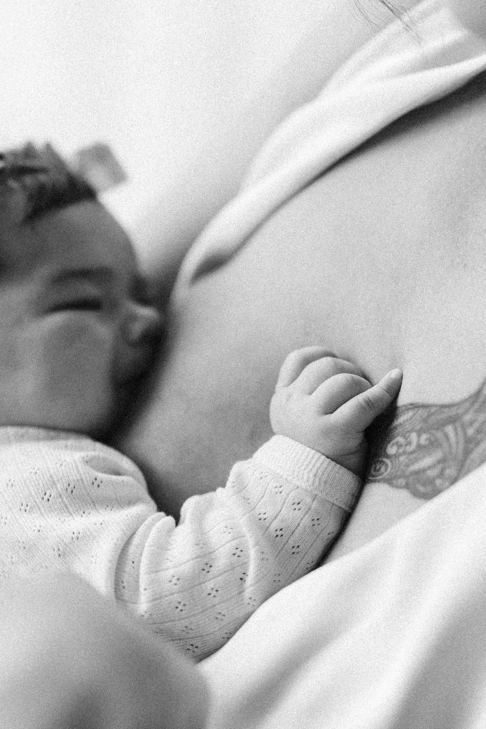 Close up black and white photo of a sleeping baby's hand resting on a soft blanket.