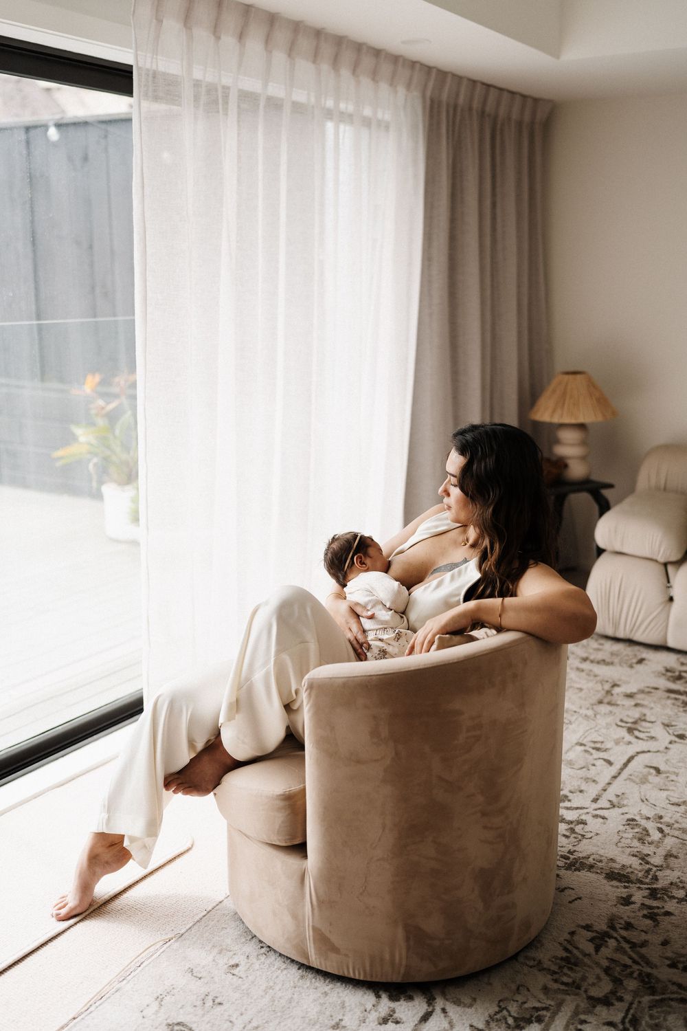 Parent nursing baby in comfortable armchair by window with natural light.