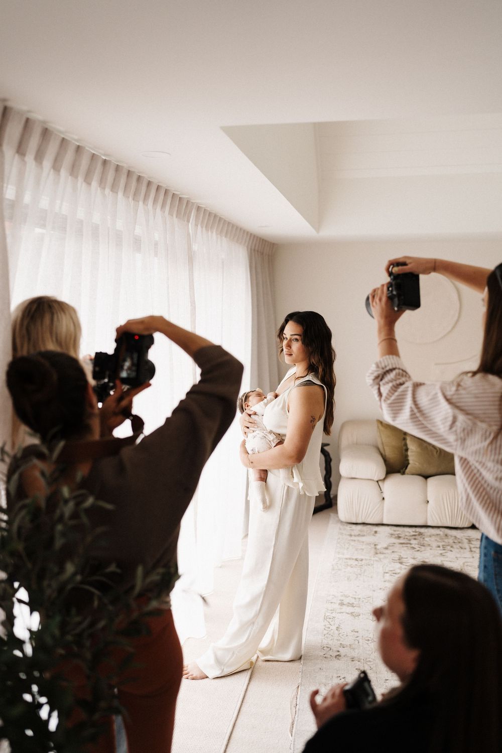 Behind-the-scenes photoshoot of parent and baby with photographers in white room.