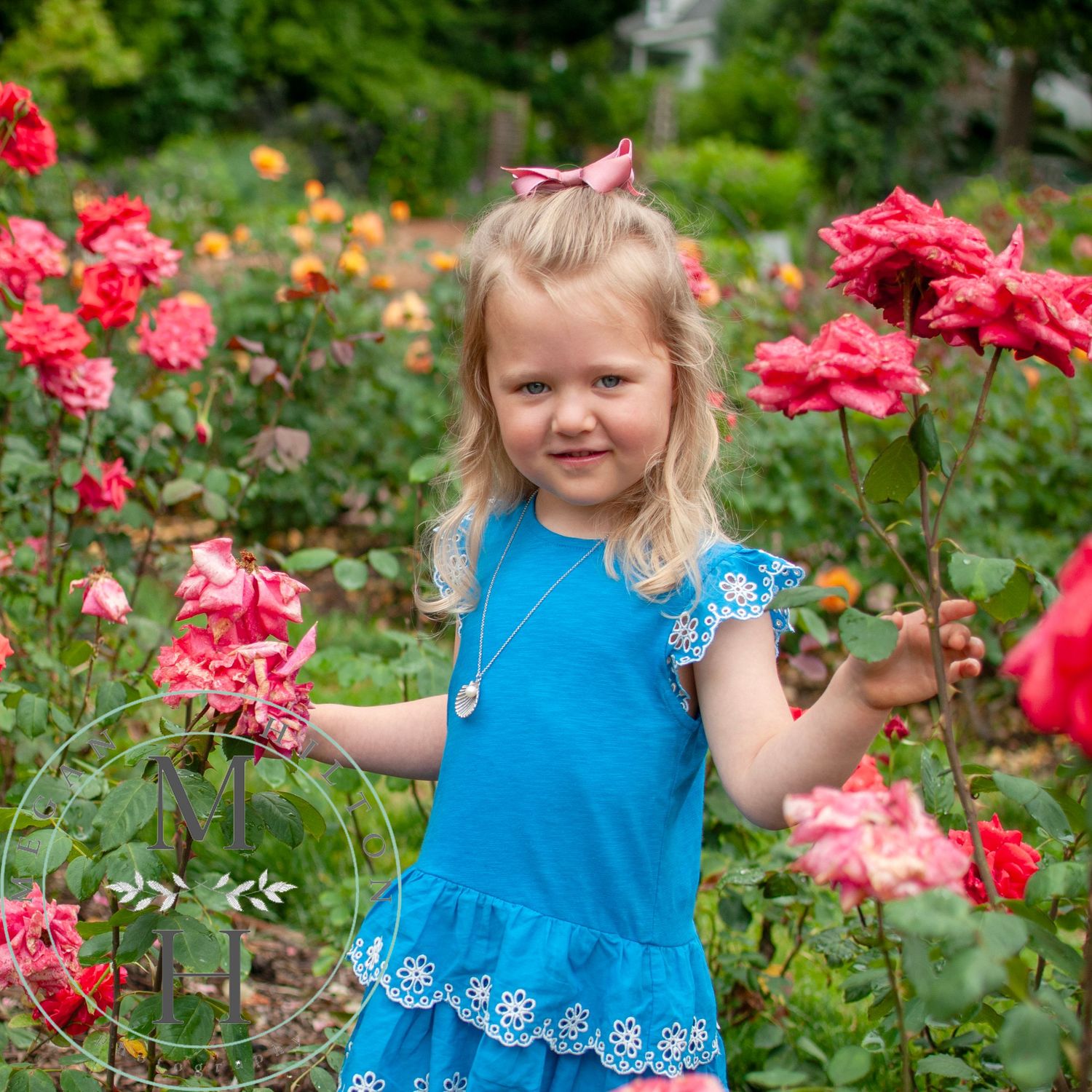 A child wearing a blue dress explores a garden filled with vibrant pink roses on a sunny summer day.