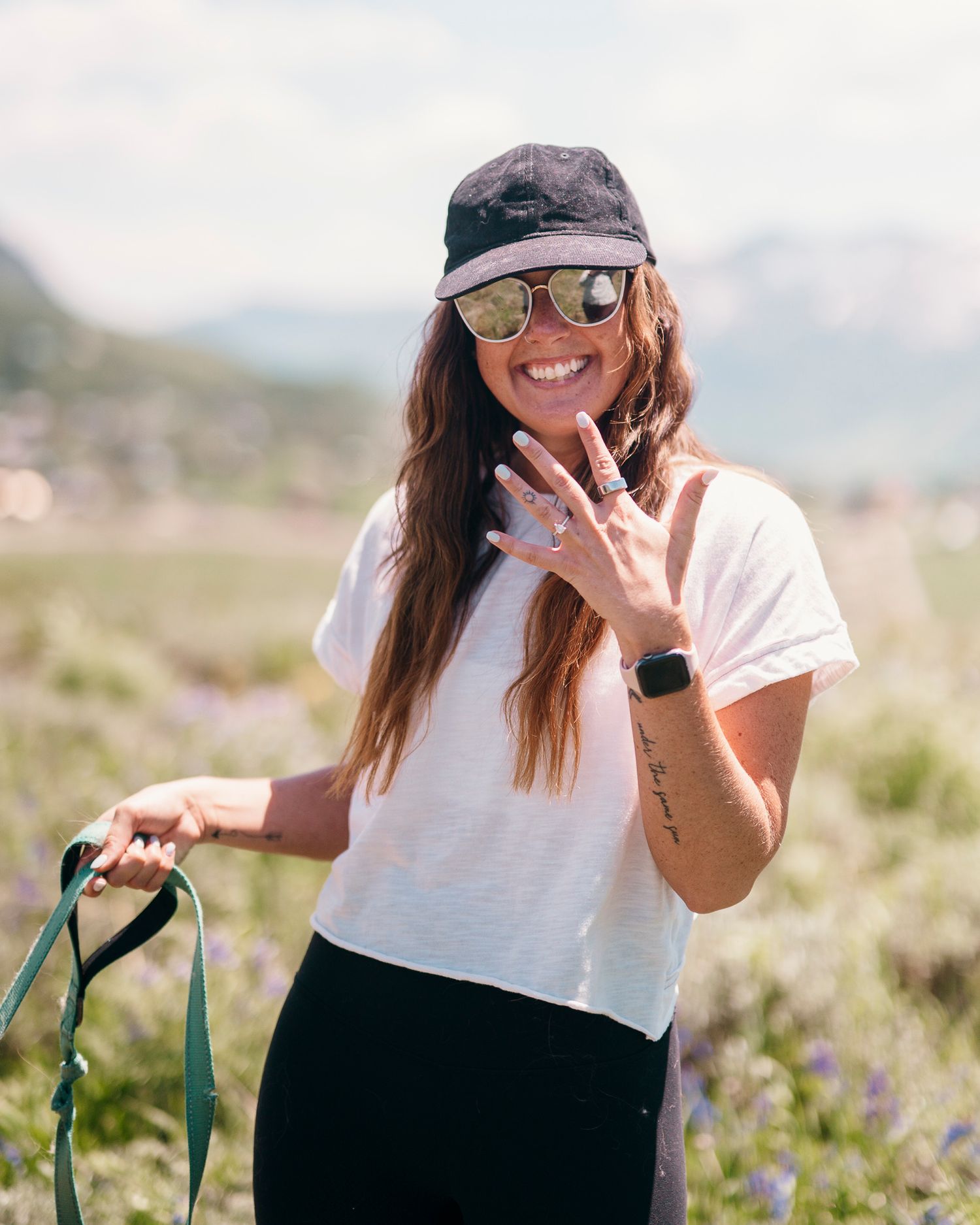 Person in white shirt and baseball cap showing excitement in mountain wildflowers.