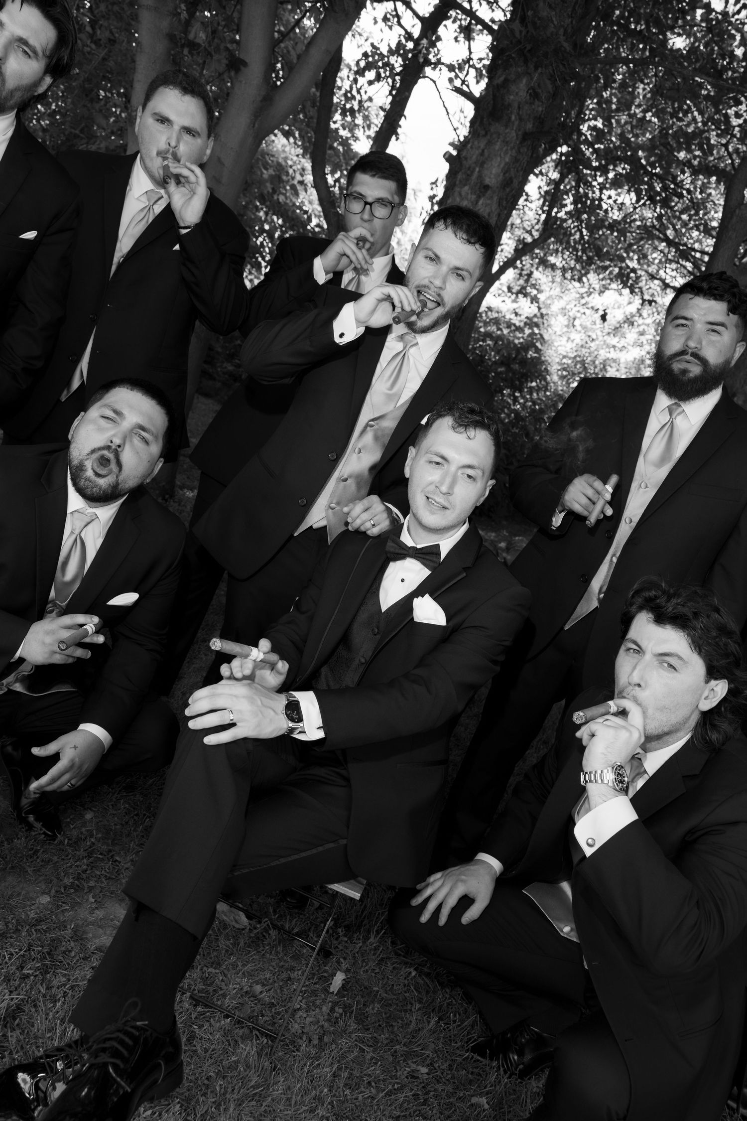 A sequence of candid photos shows groomsmen in black suits making playful and silly expressions while seated outdoors.